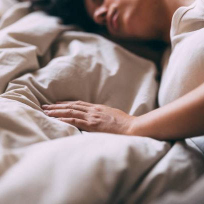 Een vrouw ligt  in bed met de hand op de dekens.