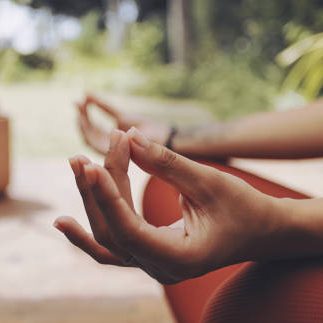Een hand in meditatieve houding met groene natuur op de achtergrond.
