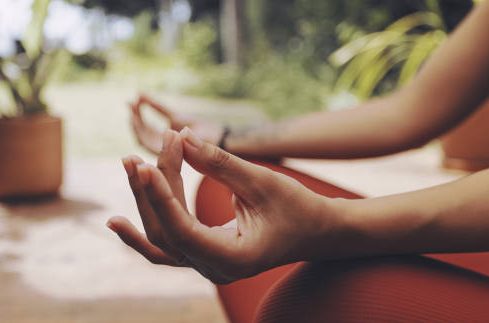 Een hand in meditatiehouding met groenere omgeving op de achtergrond.