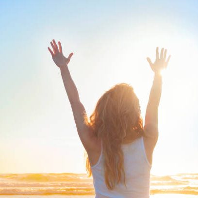 vrouw met lang haar reikt armen uit naar de zon