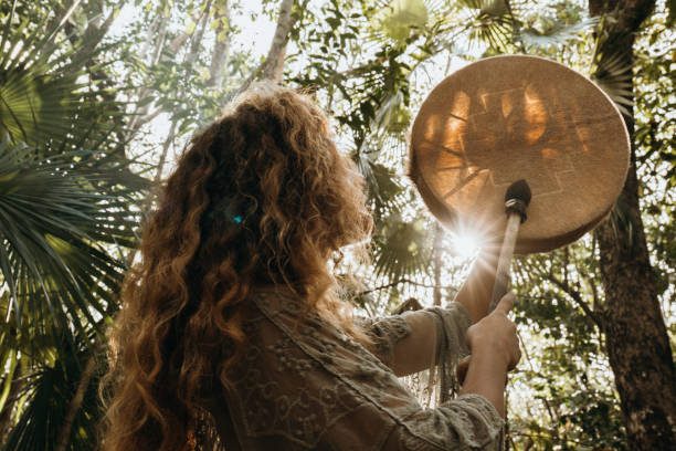 Een vrouw staat in het bos en heeft een sjamanic drum vast